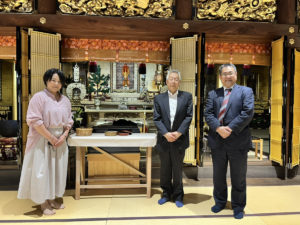 妙華寺の本堂で写真におさまる藤井奈緒理事兼アドバイザー、中川和則住職、小野木康雄代表理事（左から）